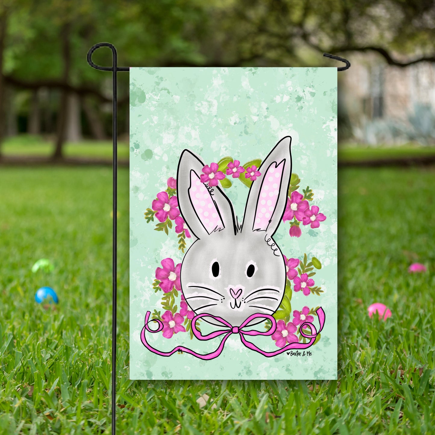 Garden flag with a cartoon bunny and flowers on a green background, placed in grass.