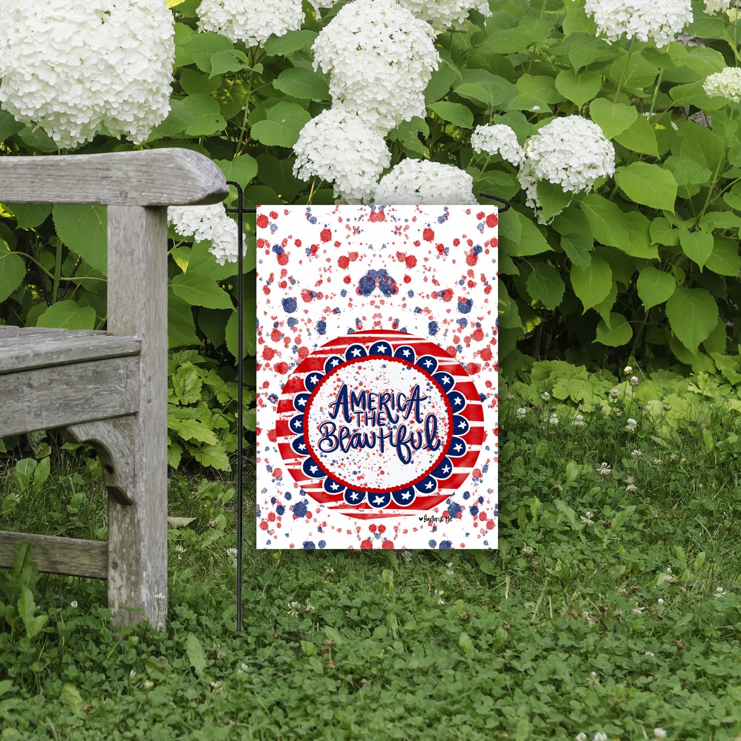 Decorative garden flag with 'America the Beautiful' design in a garden setting.