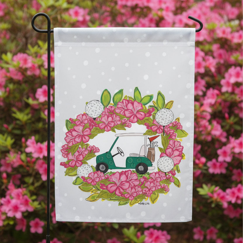 Garden flag with a golf cart and floral design in a garden with pink azaleas in the background