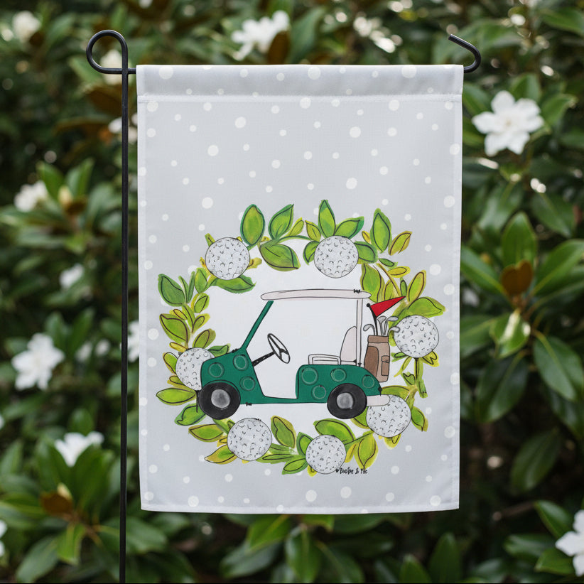 Decorative garden flag with a green golf cart and golf balls on a polka dot background - in a garden of gardenias