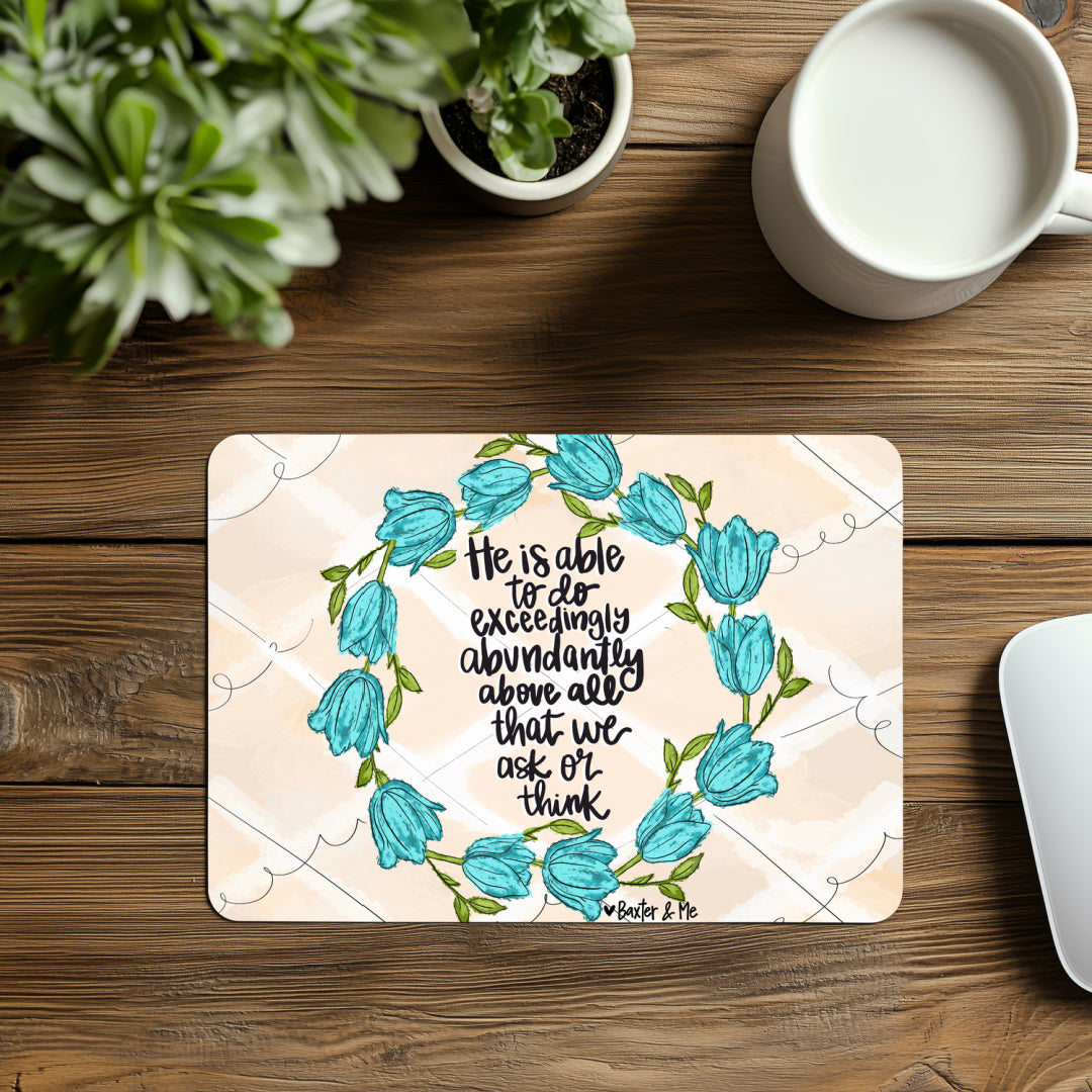 Desk with a decorative placemat featuring floral design and inspirational quote, surrounded by plants and a mug.