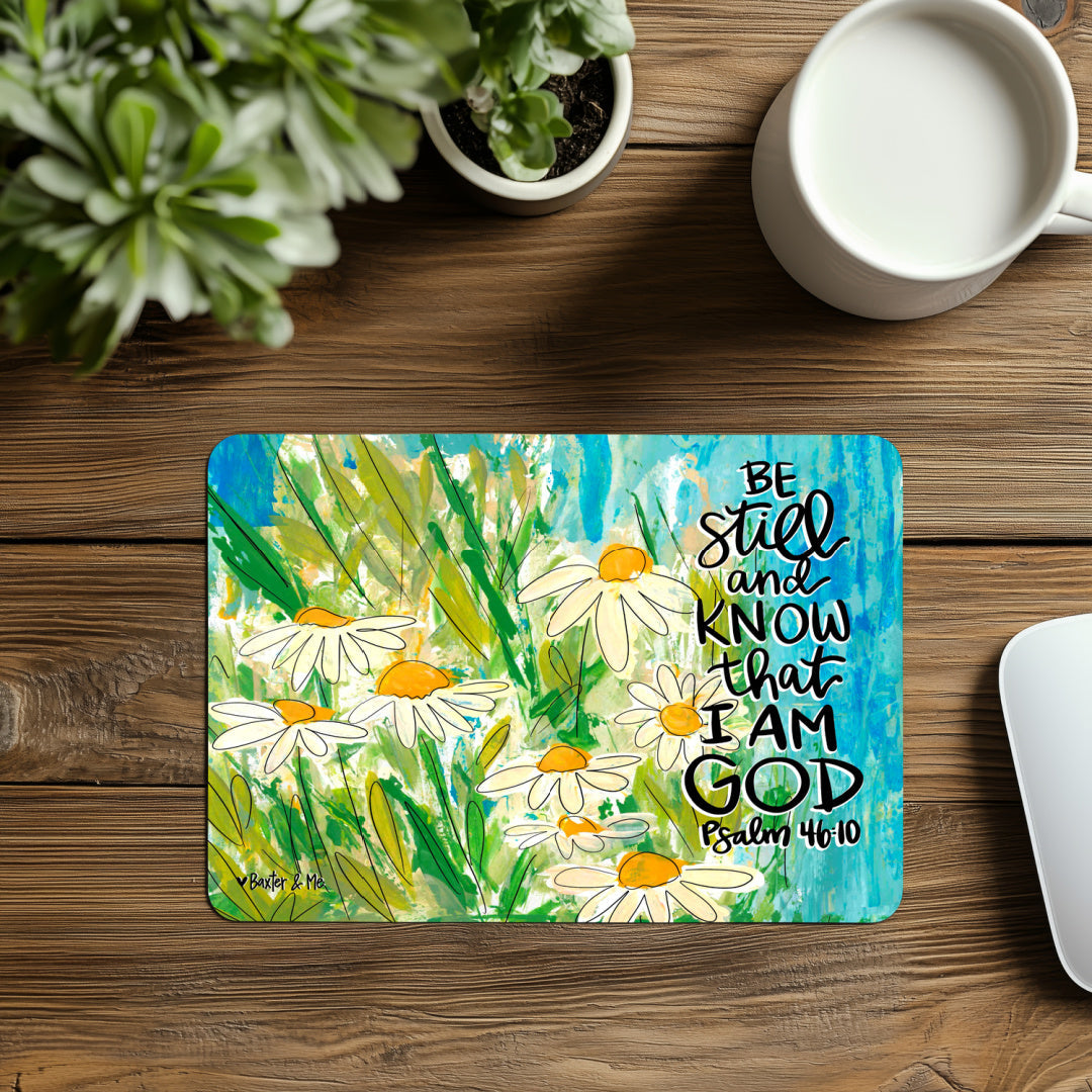 Desk setup with a decorative mat featuring flowers and text, a mug, and plants on a wooden surface.