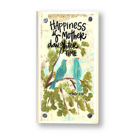 A wooden decorative plaque with a drawing of two blue birds and green foliage, with text that reads 'Happiness is in the mother's arms', 'Daughter time', and the signature of the artist.