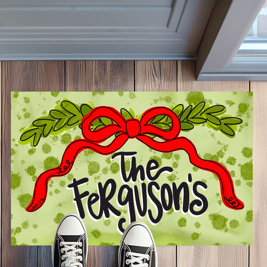Personalized doormat with a red bow and 'The Ferguson's' text on a wooden floor.