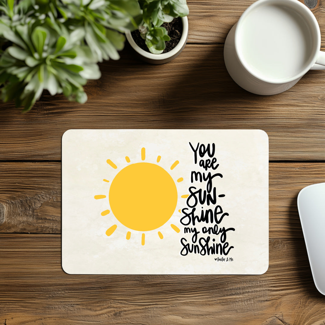 Placemat with sun design and text on a wooden table with a plant and mug.
